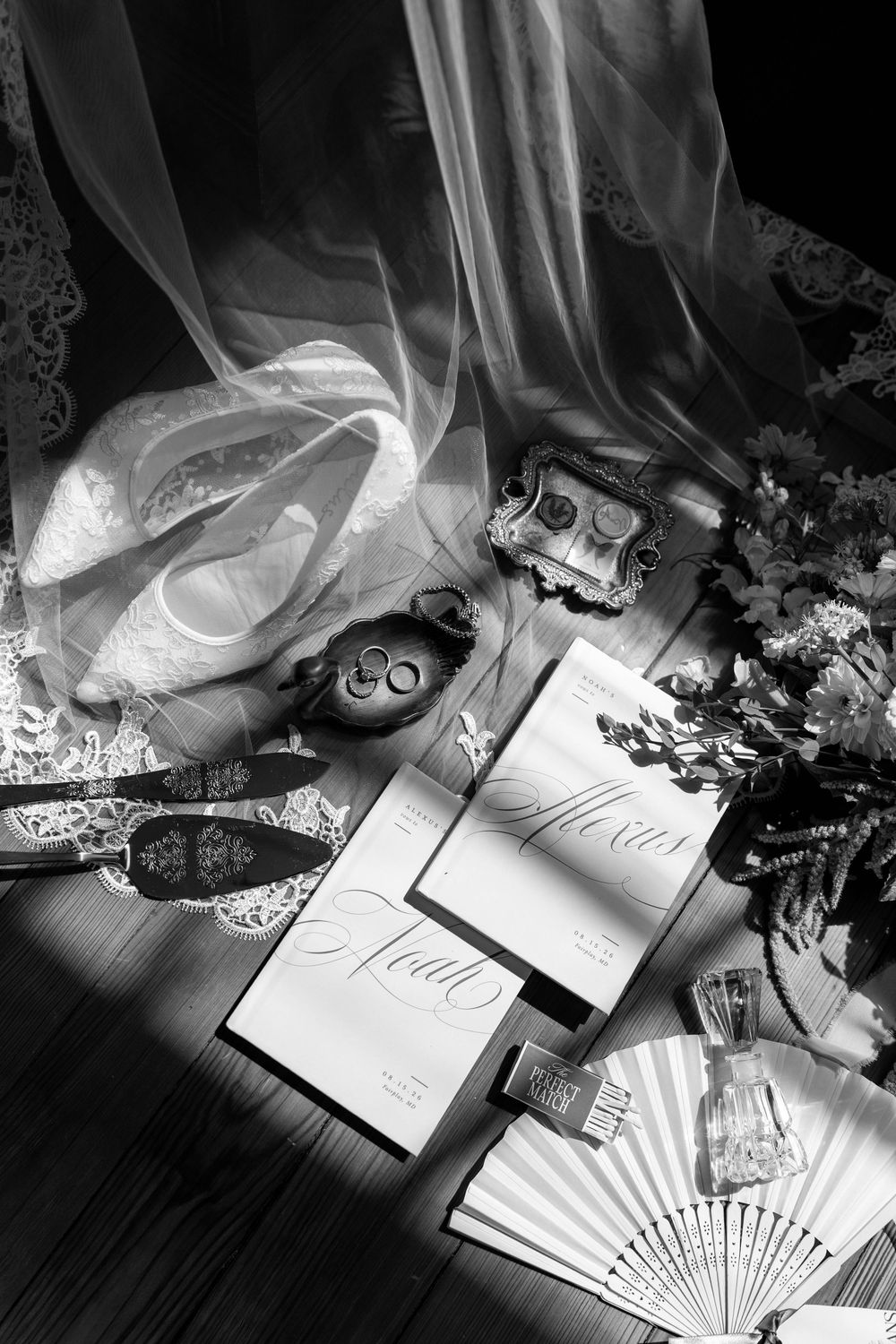 Black and white flat lay of wedding accessories including rings, invitations, shoes, and fan.