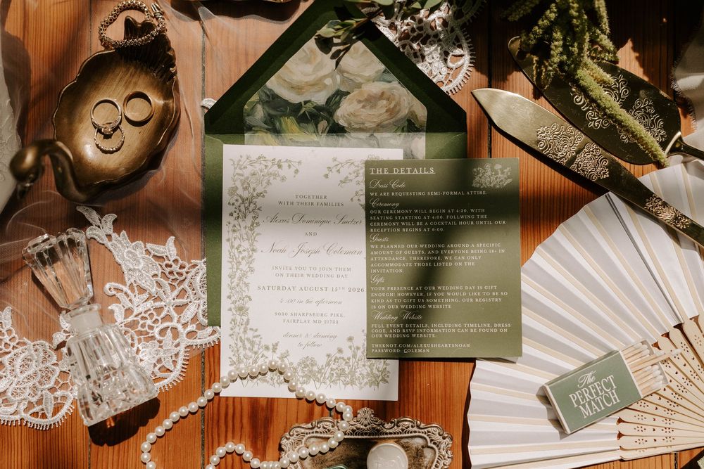 Elegant green and white wedding invitation suite with fan, rings, and lace on wood surface.