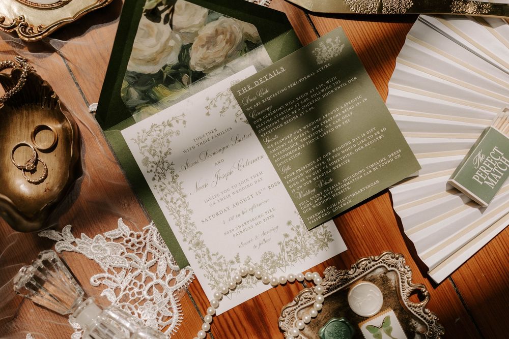 Elegant green and white wedding invitation suite displayed with rings, lace, and floral accents on wood.