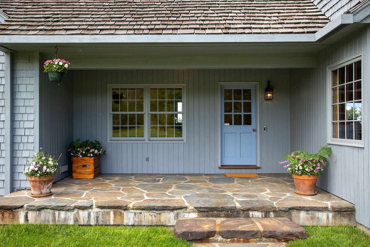 Charming light blue cottage entrance with stone patio and decorative flower pots.