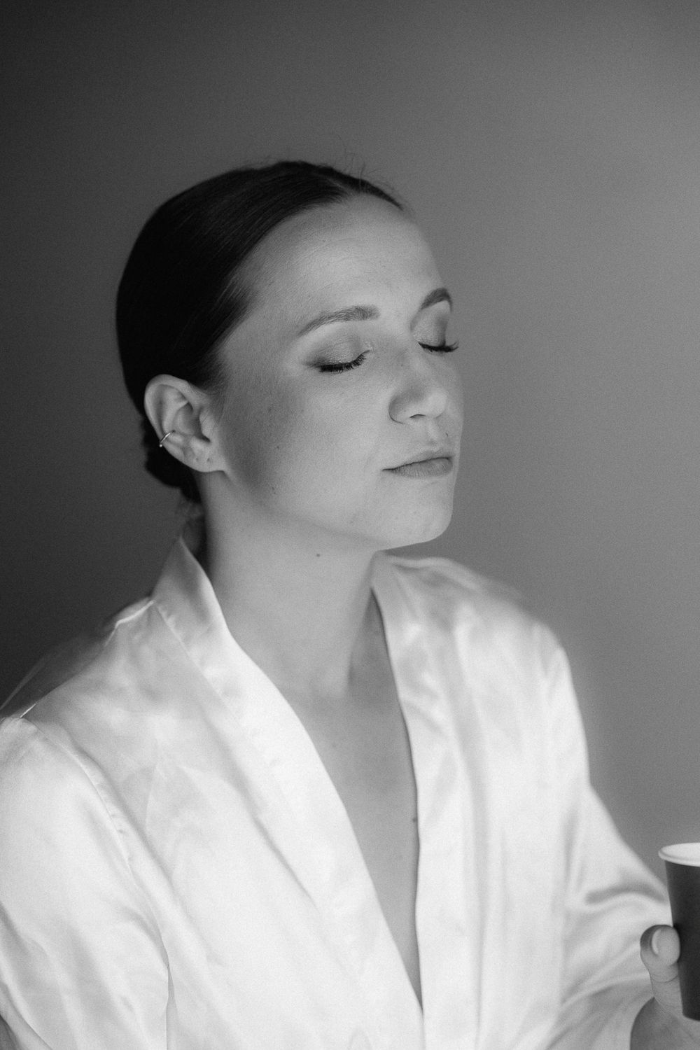 Black and white portrait of a serene woman in a white satin robe holding a cup with eyes closed.