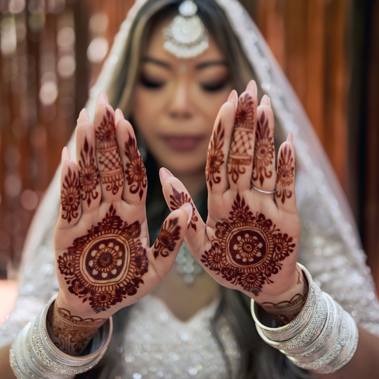 Bride in white lehenga displays intricate henna mehndi designs on both palms at her wedding ceremony.