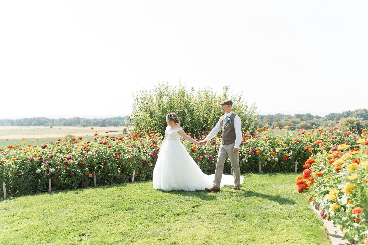 Couple holding hands running through tall grass field toward lush green forest trees outdoors.