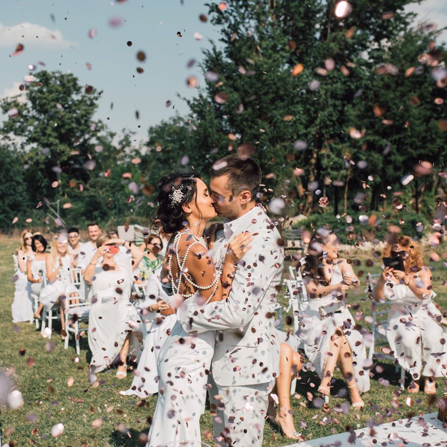 A couple strolls through vineyard rows during golden hour in elegant wedding attire.