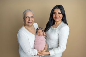 Three generations of women pose together, with grandmother and mother holding a swaddled newborn baby in a pink wrap.