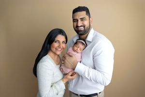 New parents smiling and holding their swaddled newborn baby in a professional studio portrait.