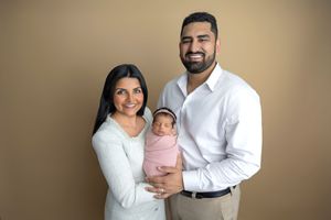 Happy couple posing with their pink-swaddled newborn in a warm-toned studio family photo.