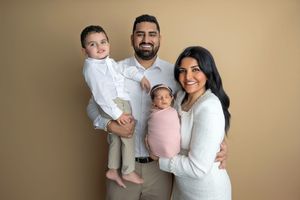 Happy family of four posing for a portrait, parents holding toddler son and newborn baby girl in pink wrap.
