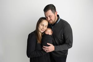 New parents tenderly hold their swaddled newborn baby during a professional studio portrait session.