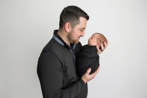 Father gazes lovingly at his swaddled newborn baby during a professional studio portrait session.