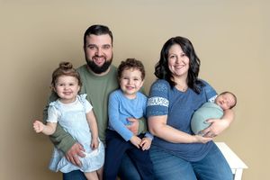 Family of five posing for a professional portrait, parents with two toddlers and a newborn baby, against a tan background.