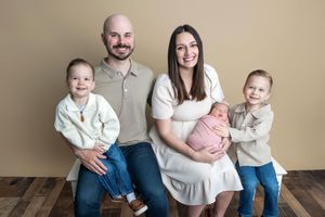 A happy family of five poses for a professional portrait, with parents holding their newborn and two young children smiling.
