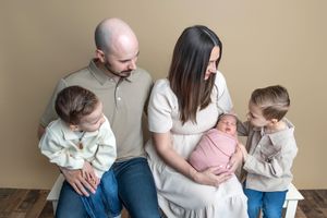 Family of five with newborn baby in pink wrap, parents holding children in a warm studio portrait.