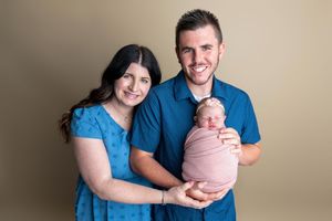 Smiling couple holding their newborn baby wrapped in pink during a professional studio portrait session.