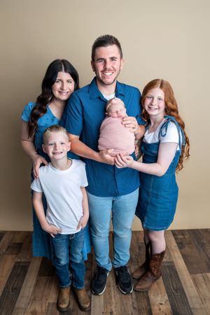 Family of five posing for a studio portrait, parents with two children and a newborn baby wrapped in pink.