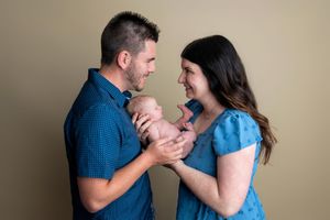 Parents in blue outfits smiling at their newborn baby during a professional studio portrait session.