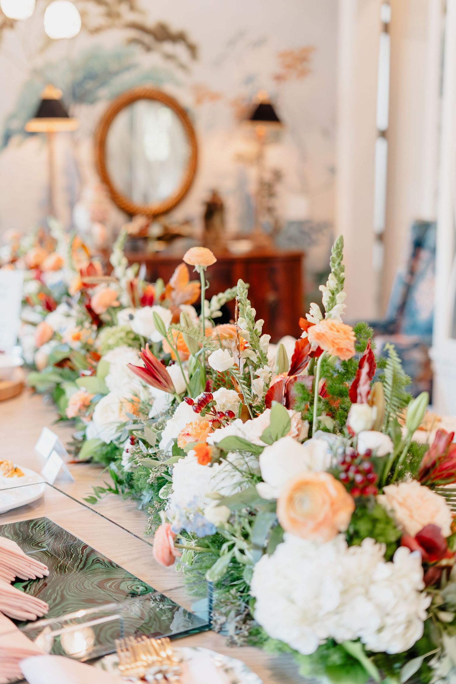 Elegant floral table runner with white, peach, and red blooms at a styled dining table setting.