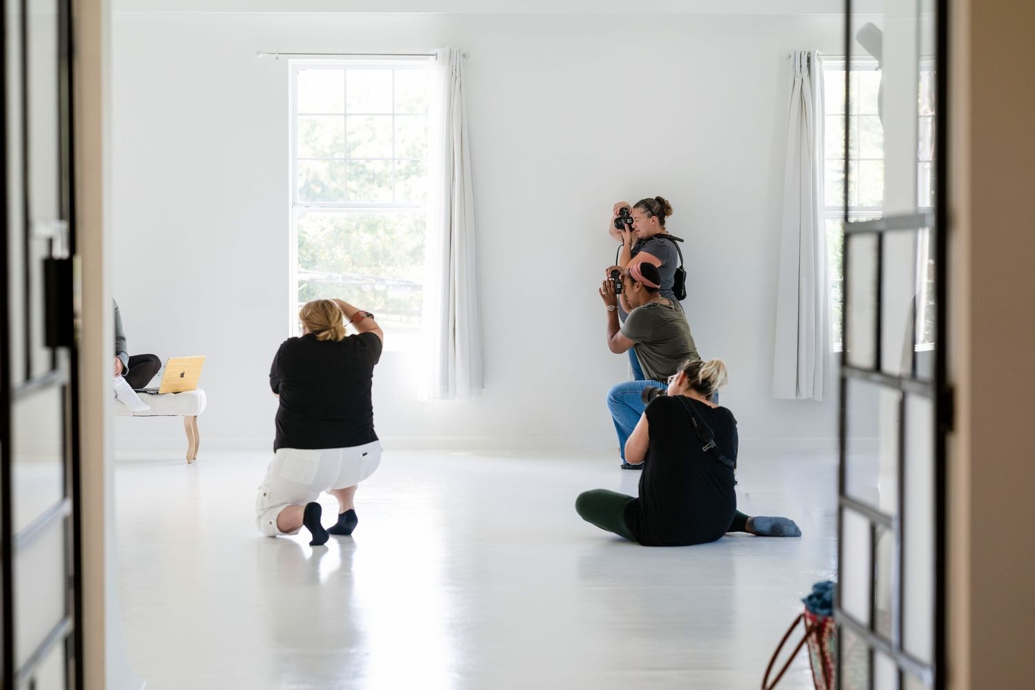 Photographers capturing a model in a bright white studio with large windows during a professional photo shoot.