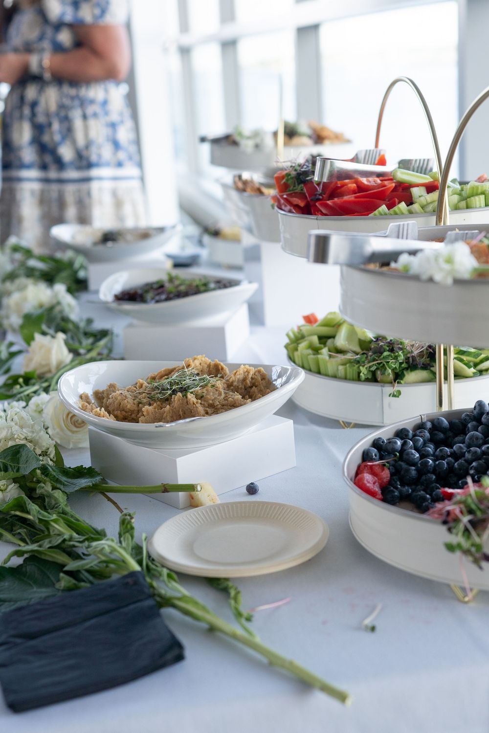 Elegant wedding buffet table with fresh fruit, vegetables, and appetizers displayed in white serving dishes.