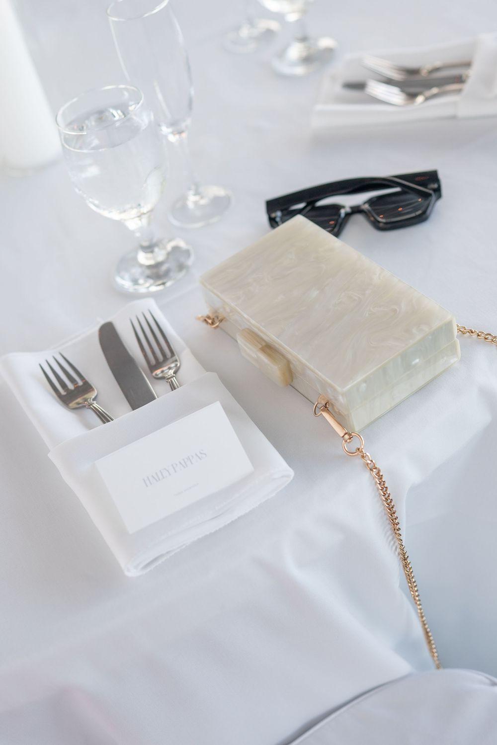 Wedding table setting with pearl clutch purse, place card, silverware and glasses.