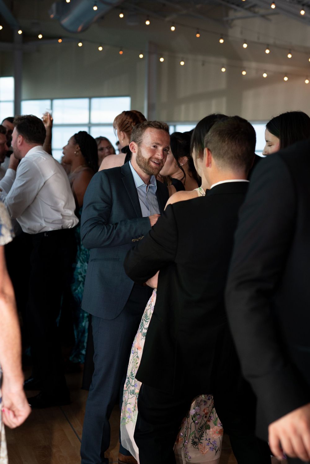 Wedding guests smile and dance together on the reception dance floor under warm string lights.