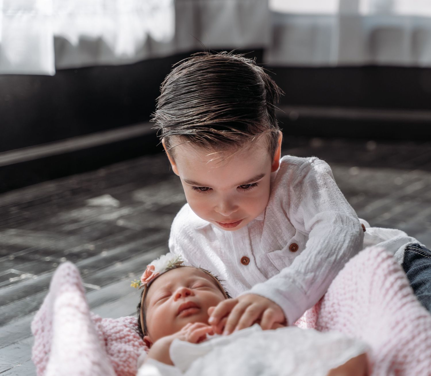 Big brother gently touching his newborn sister during a newborn family photography session.