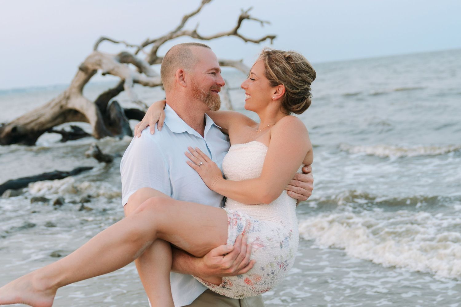 Rachel and Bo sit together on the beach during their Driftwood Beach engagement photos