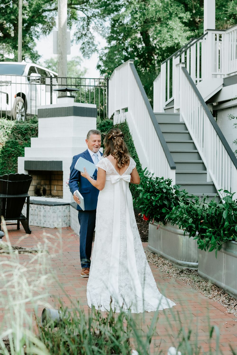 Bride and groom share first look moment in lace wedding gown and navy suit outside elegant venue with brick pathway.