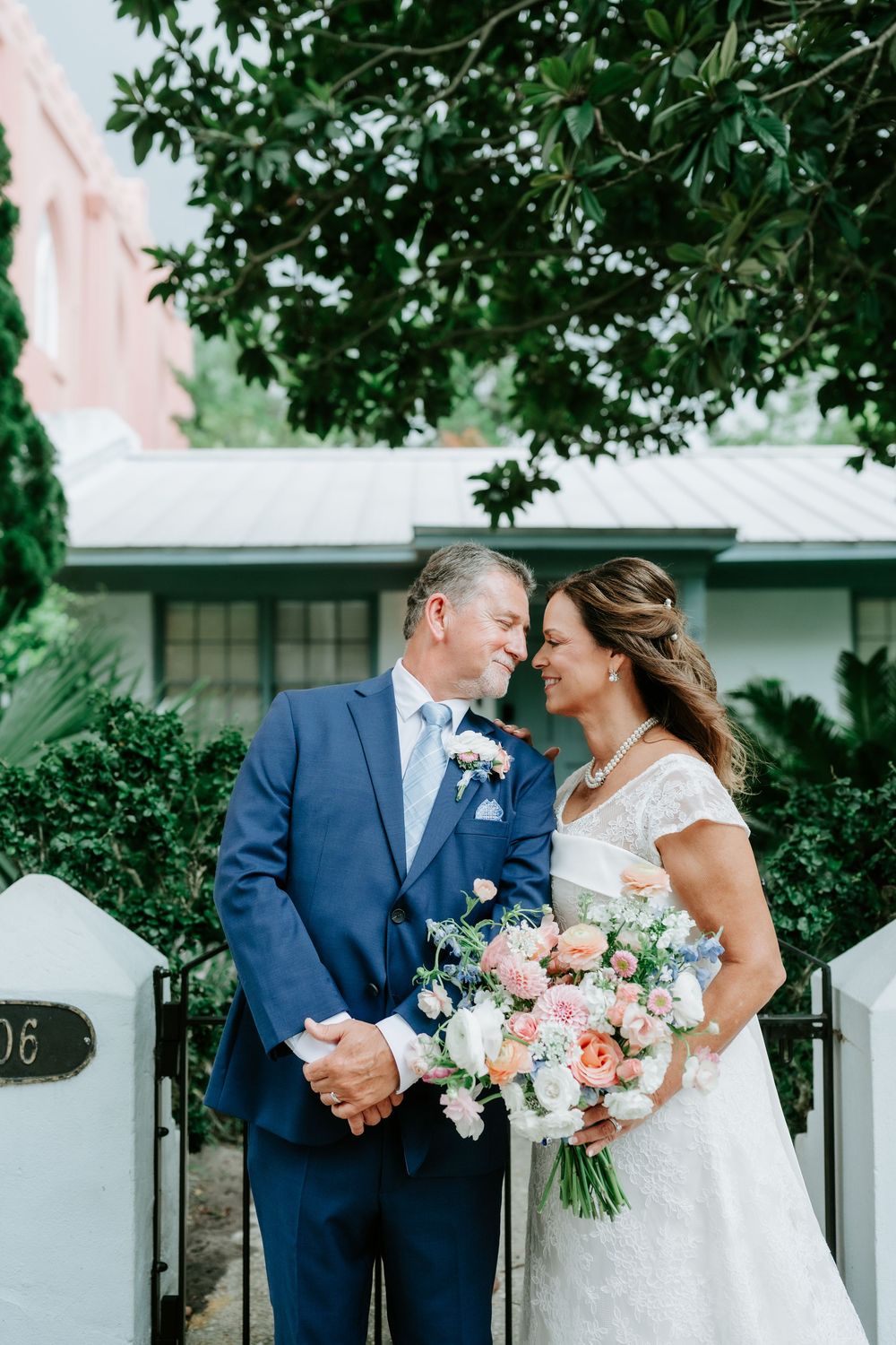 Bride and groom share a romantic nose-to-nose moment outside a historic home, bride holding a beautiful pastel bouquet.