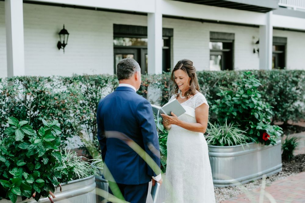 Bride and groom exchange vows outdoors at elegant venue surrounded by lush greenery during wedding ceremony.