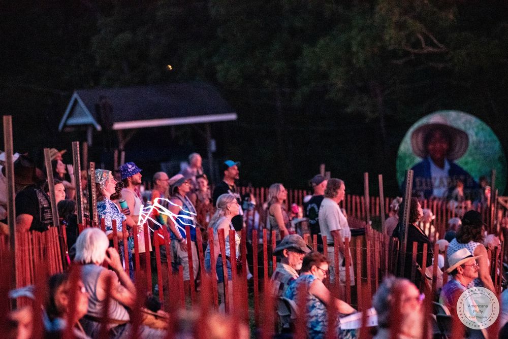 Large crowd gathered outdoors at night, illuminated by red lights, attending an open-air cultural festival event.