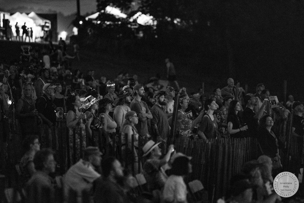 Black and white photo of a large crowd at an outdoor music festival at night.