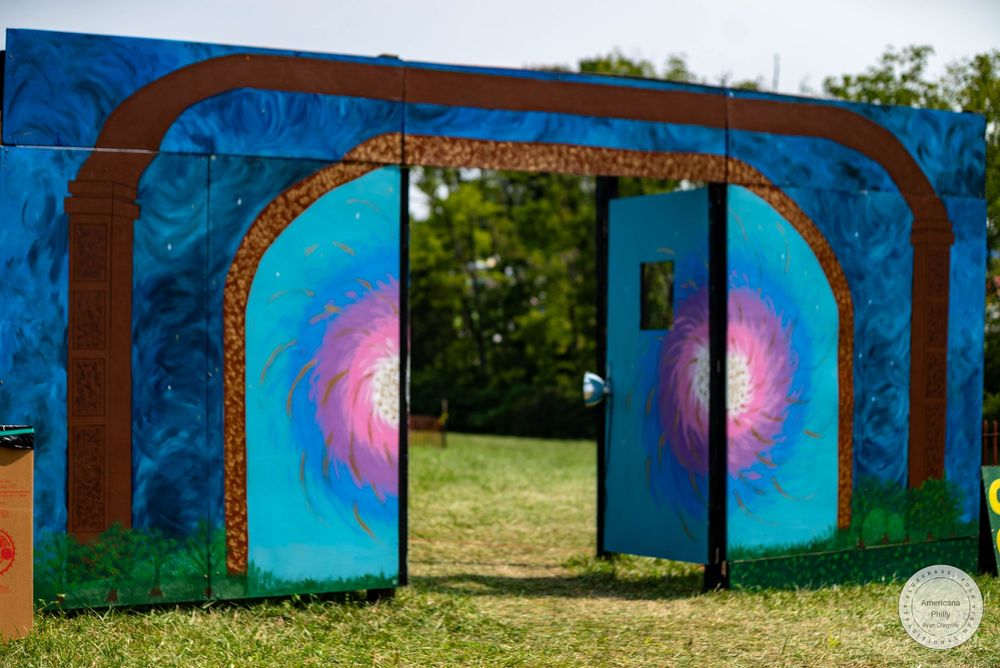 Colorful outdoor art installation with painted arched doorways featuring blue and pink swirling murals on a grassy festival grounds.