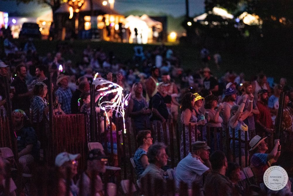 Crowd enjoying an outdoor night festival with glowing light spinners and colorful illuminated decorations in the background.