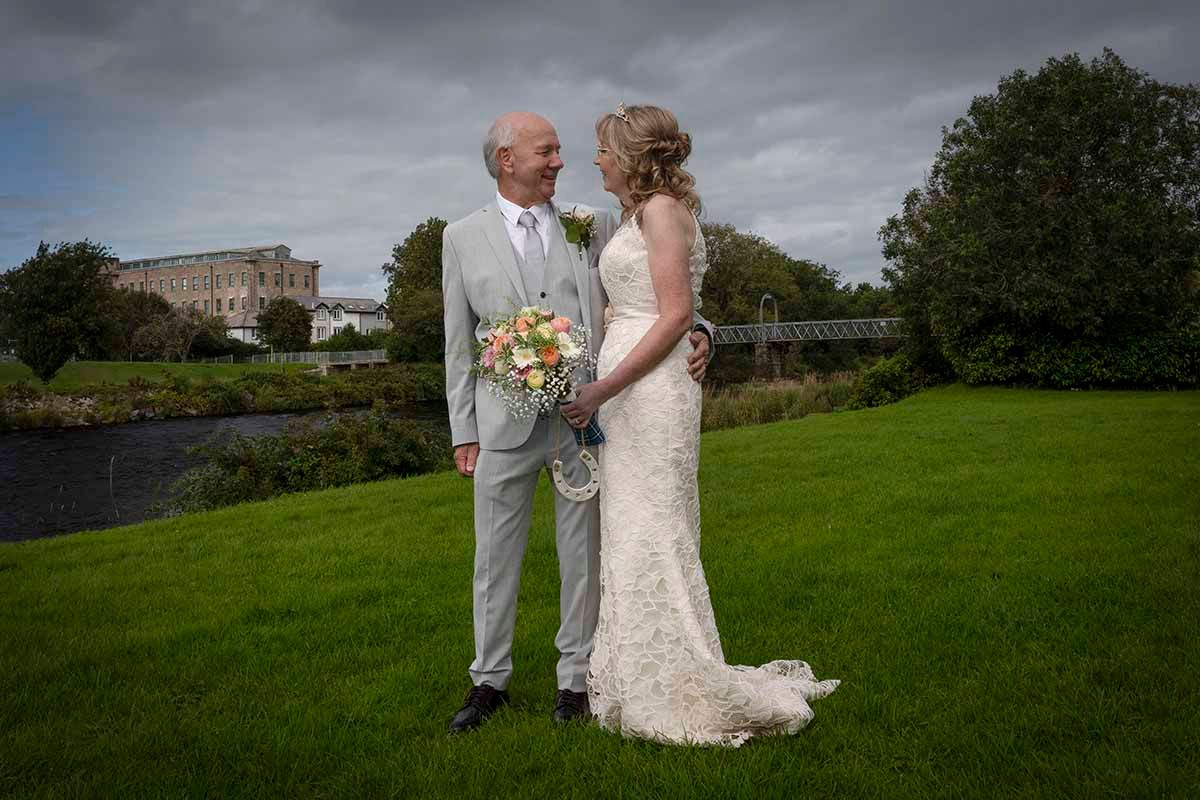 Bride and groom on the lawn outside the Trout Hotel in Cockermouth with the river Cocker in the backdrop on their wedding day.