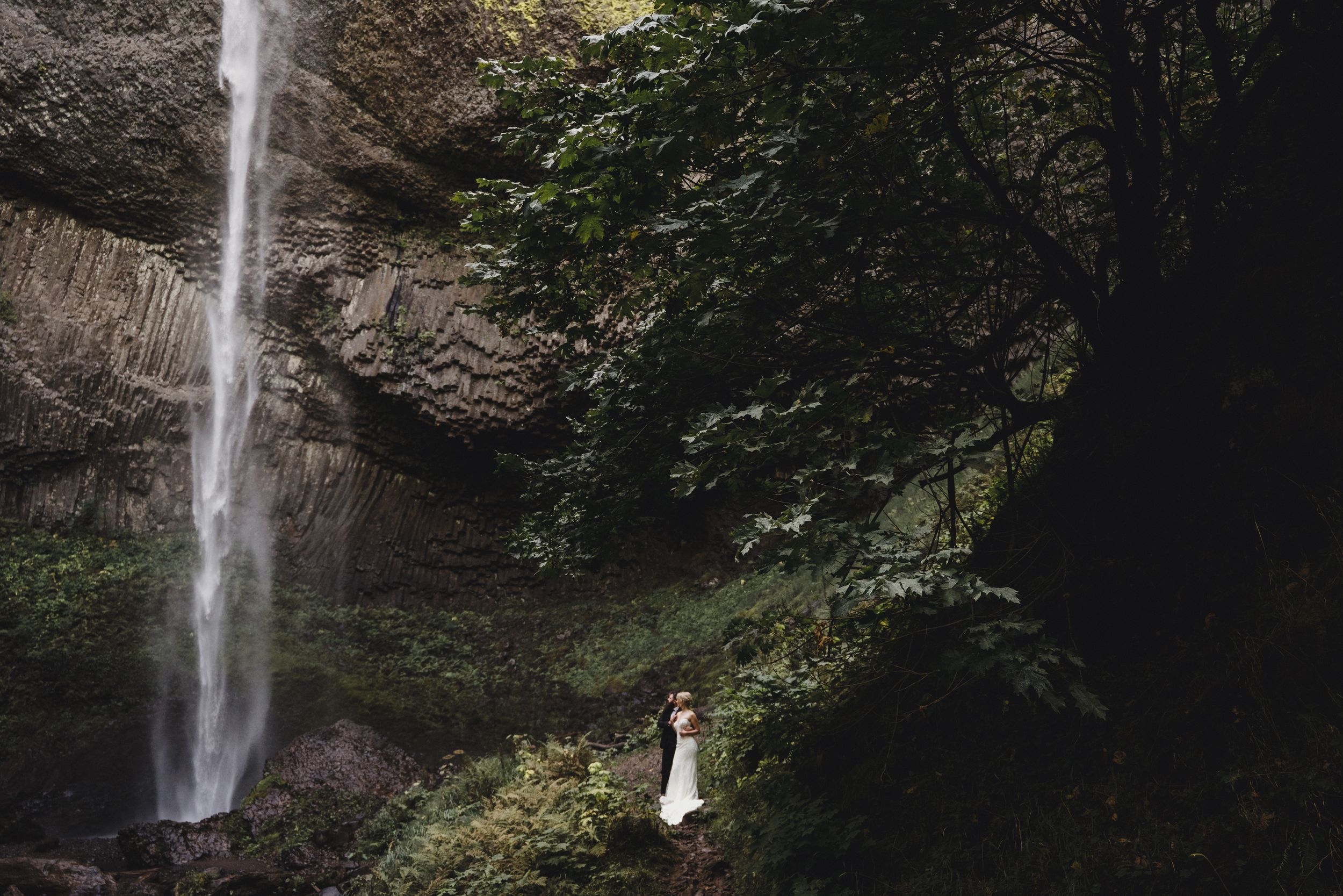 Eloping couple at Latourell Falls in Oregon, surrounded by lush green trees and mossy basalt rock in the gorge.