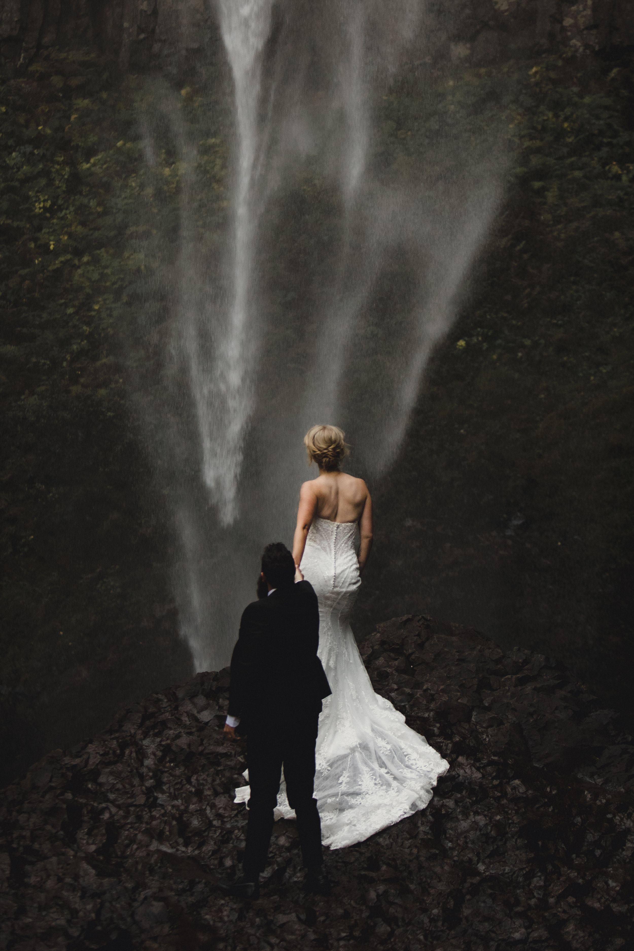 Elopement where bride reaches up to touch the spray from the PNW waterfall