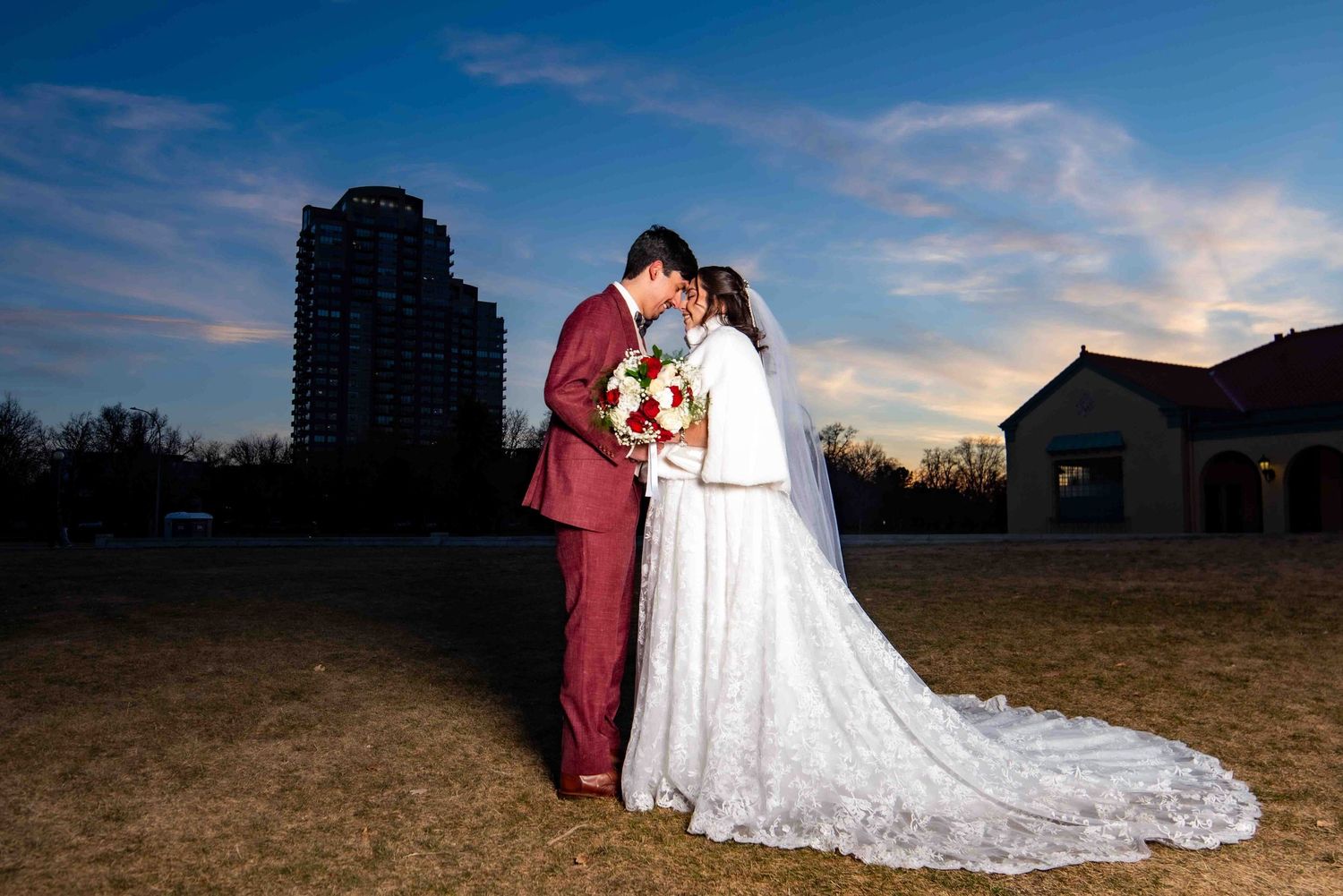 A newlywed couple shares a romantic moment at dusk with a city skyline in the background.
