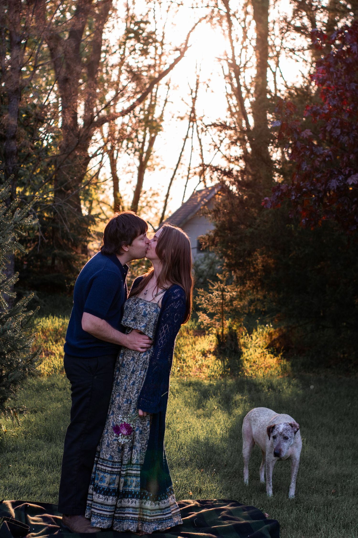 A couple lovingly gazes at their newborn baby wrapped in a blanket with a yellow bow headband near a sunlit window.