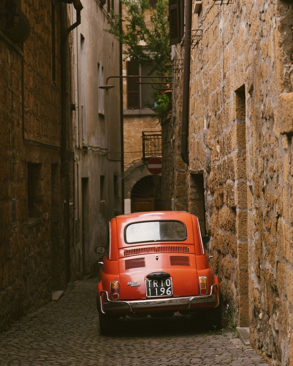 Little red Fiat parked in a narrow stone alley in Tuscany