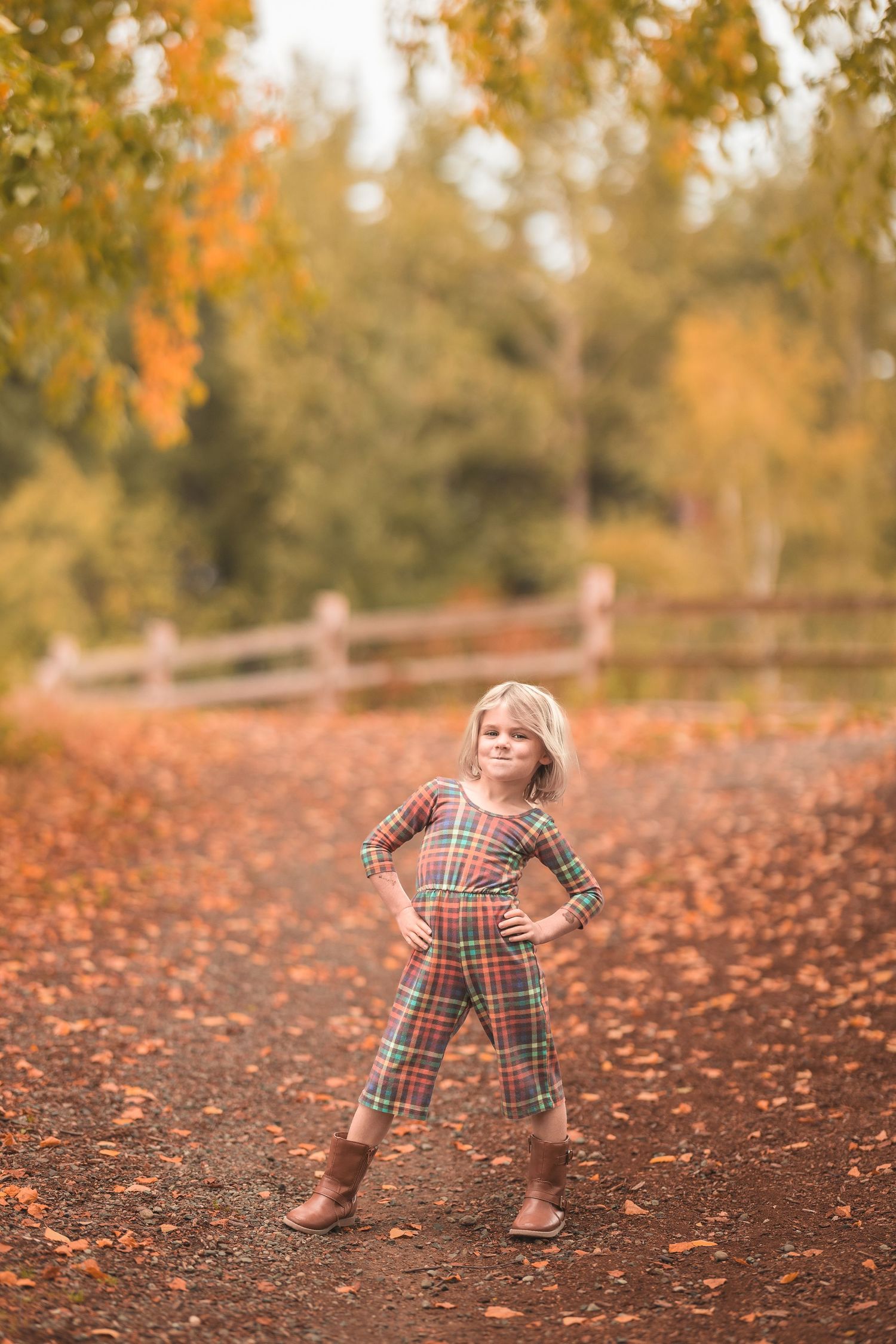 Two boys and a toddler girl in autumn outfits hold hands smiling outdoors with fall foliage and mountains.