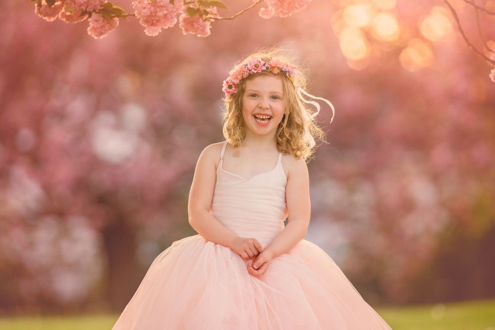 Young girl smiling beneath blooming cherry blossom trees during a spring portrait session in Cherry Hill, NJ.