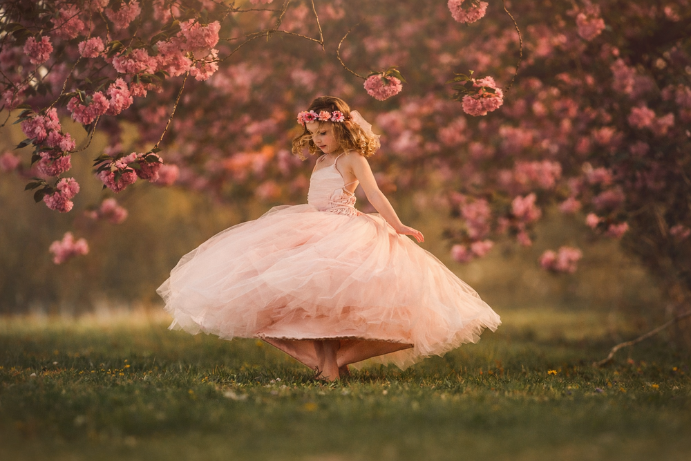 Young girl twirling beneath pink cherry blossoms during a spring photography session in Cherry Hill, New Jersey.