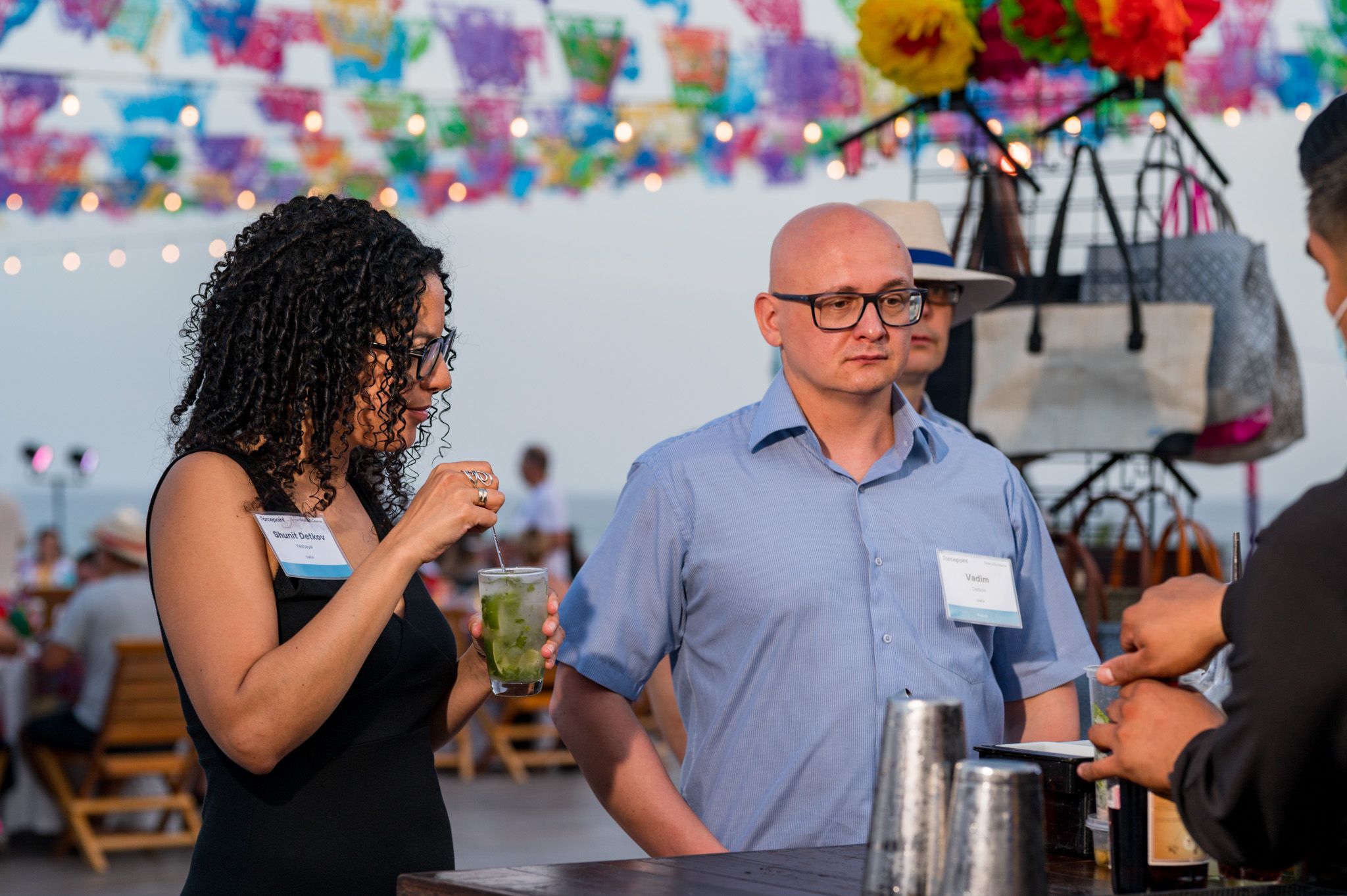 Two professionals wearing name tags engage in conversation at a festive outdoor networking event with colorful decorations.