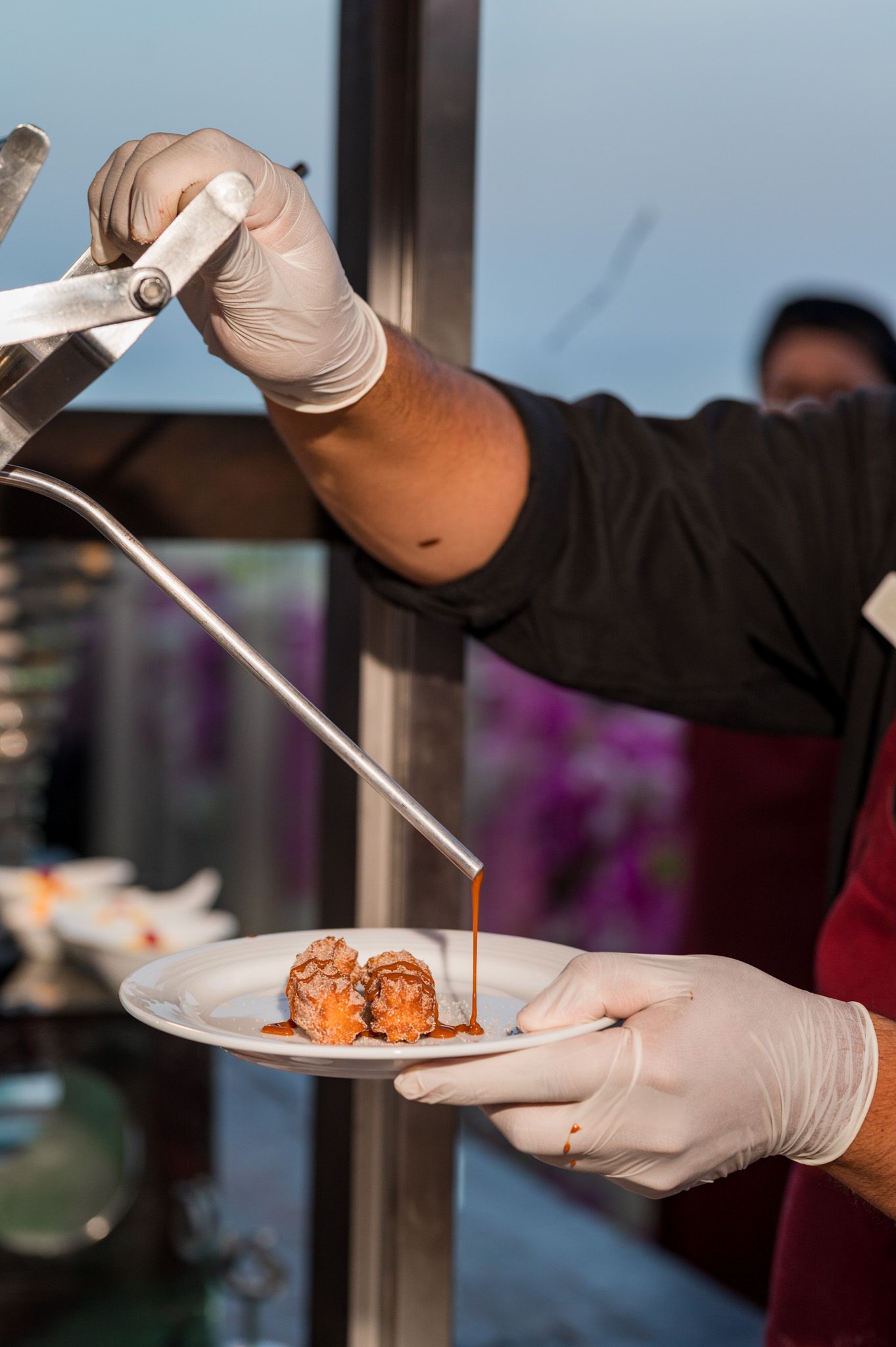 Chef in gloves drizzling rich brown sauce over plated sushi rolls at an upscale restaurant.