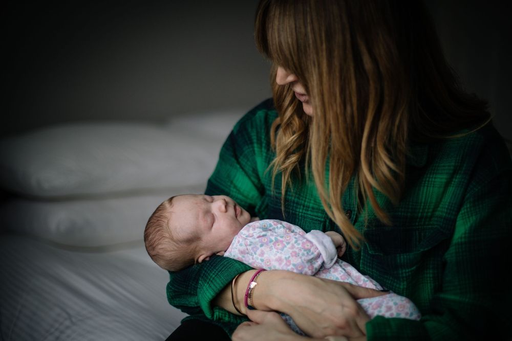 A mother in a green sweater gently cradling her sleeping newborn baby.