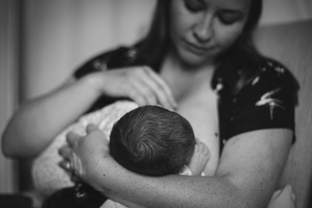 Black and white photo of a mother tenderly cradling her newborn baby in her arms.