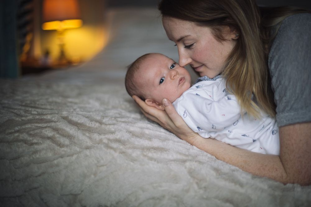 A tender moment as a young mother gazes lovingly at her newborn baby lying on a soft white blanket.