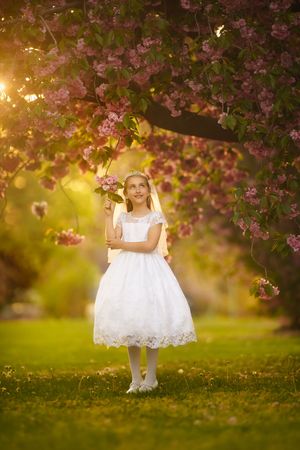 Young girl posing among blooming cherry blossoms during her First Holy Communion portrait session.