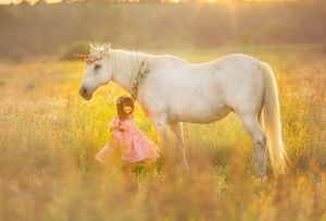 Young girl posing with a unicorn in a field at sunset during a fine art fantasy portrait session.